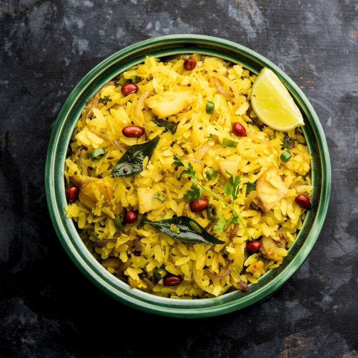 Kande Pohe OR Aloo Poha is a popular Indian breakfast recipe made using Flattened rice, usually served with hot tea. Served in a bowl over moody background. Selective focus