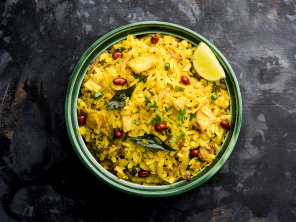 Kande Pohe OR Aloo Poha is a popular Indian breakfast recipe made using Flattened rice, usually served with hot tea. Served in a bowl over moody background. Selective focus